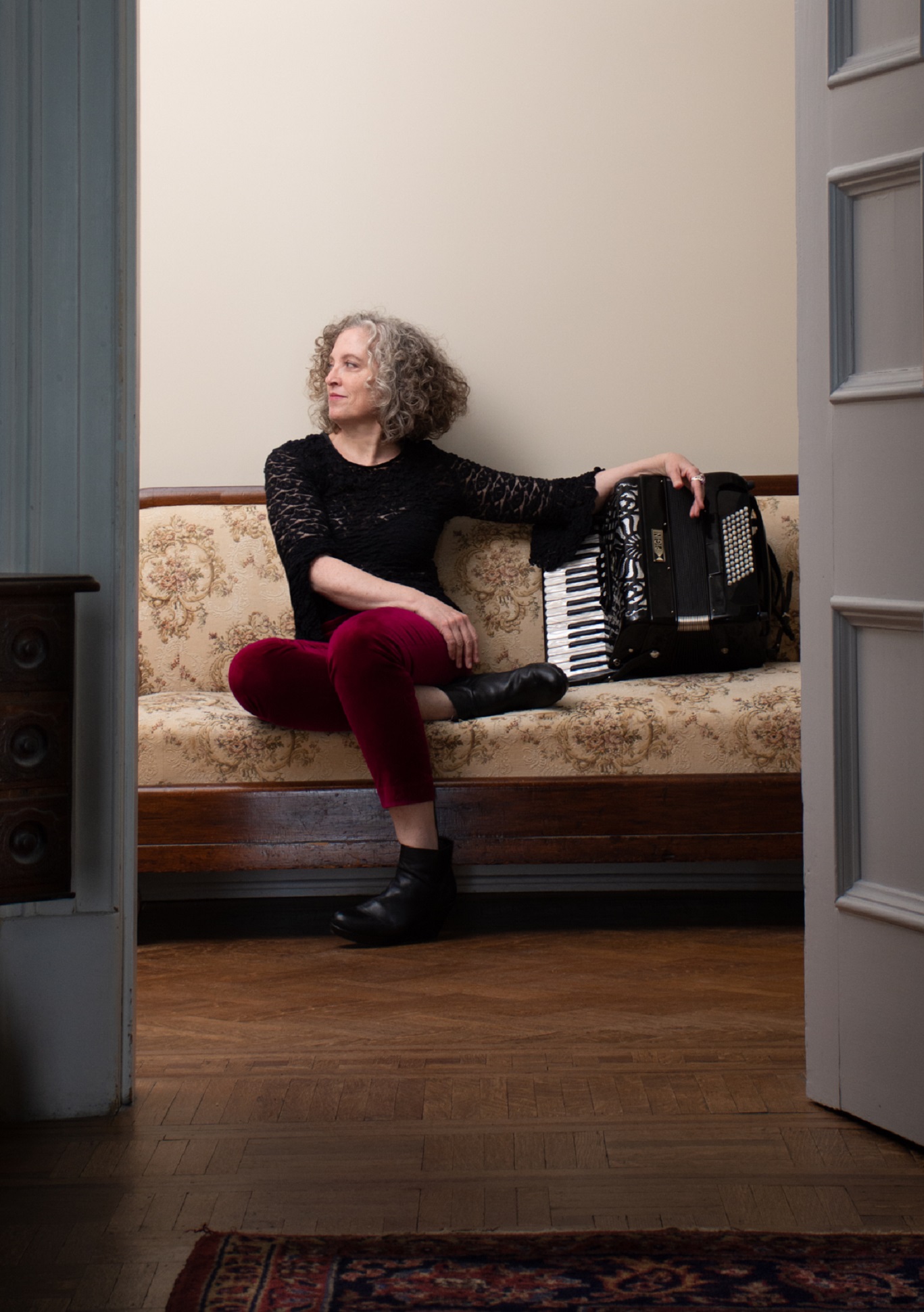 A photo of Jan LeClair through a door sitting on a couch beside an accordion.