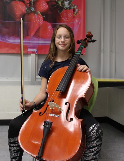 Dayah Rego poses with a cello while seated in a classroom