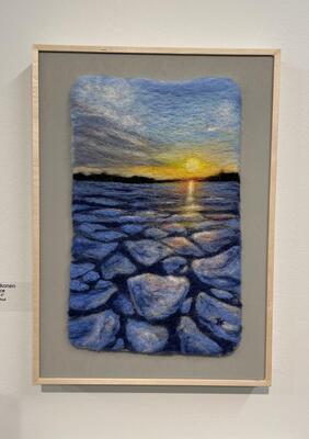 A photo of a needle felted scenerey on display in a frame. The scene shows a lake with floating piece ofice