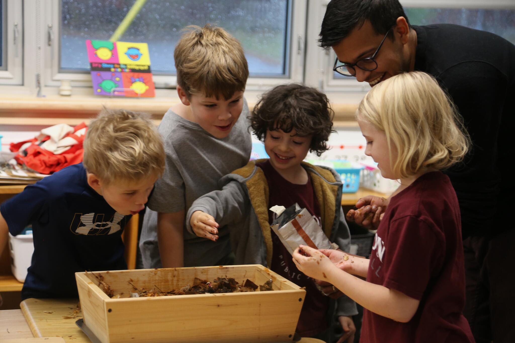 4 students and an adult gather around a worm box in a classroom 