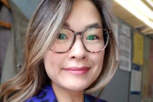 Sandra smiles at the camera. She is wearing a purple blazer and glasses