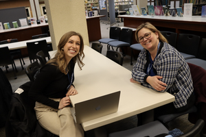 Erica Lewick and Nathalie Soini look st the camera smiling while sitting at a table in the Education library 