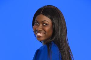 Ann smiles over her shoulder at the camera wearing a blue dress. She has long dark hair