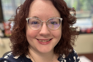Katherine smiles at the camera wearing bejeweled glasses and a striped cardigan.