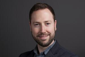 Mark Richardson poses in front of a grey background wearing a blazer.