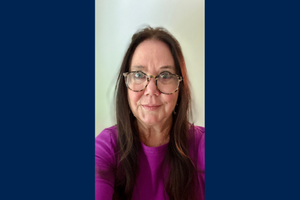 Erin Kelly smiles wearing a purple shirt and glasses.