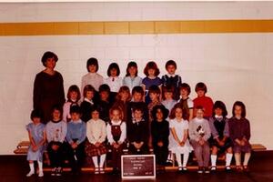 Maureen Watkin poses to the left of her class in a class photo with students sitting on the bleachers.