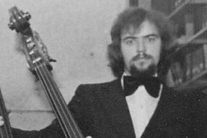 Roger Finlay in a photo from his time at school wearing a bowtie and suit and holding the neck of a cello.