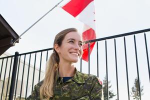 Elyse O'Brien wears a camouflage uniform and stands in front of a Canadian flag.