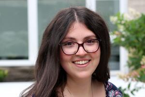 Alexandra Bosco smiles outside, she wears glasses and a purple floral shirt.