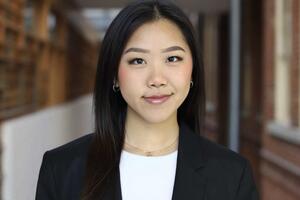 An Asian woman wearing a white shirt and a Blazer smiling in a library