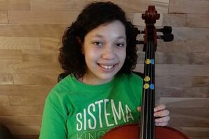A girl in a green shirt sits holding a cello