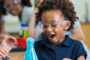 Two Black children smile while performing a science experiment with safety glasses on