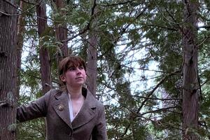 An image of a woman hovering in a forest in an overcoat