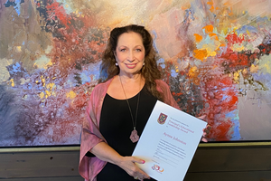 Aynne Johnston smiles and holds an award in front of a colourful background