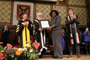Rosalie Griffith smiles as she receives a framed award on stage at a graduation ceremony.