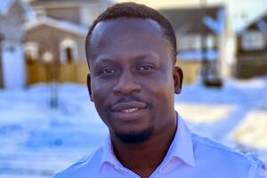 Kenneth Gyamerah smiles outside wearing a white collared shirt with a snowy background.