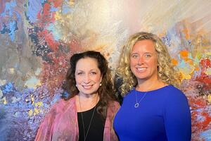 Aynne Johnston and Michelle Searle smile against a colourful backdrop.