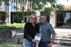 Kerstin Merz-Atalik and Ted Christou pose with a copy of their book outside.