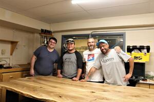Students gather around a completed wooden table that was part of a class project.