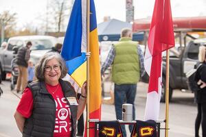 Lynda Colgan poses outside next to a rolling robot that holds a Queen's flag.