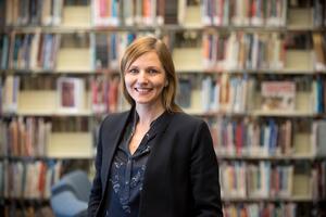 Pamela Beach stands in front of a book shelf smiling