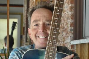 Gary holds guitar and smiles at camera 