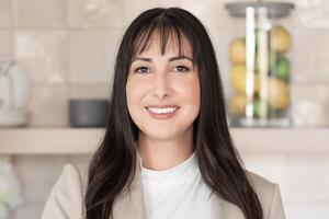 A woman stands in a kitchen with a khaki blazer on 