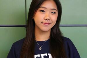 Rachel Su wearing a blue Queen's sweatshirt with a green background