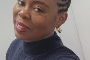 A black woman smiles at a camera with a black turtleneck on and a white background
