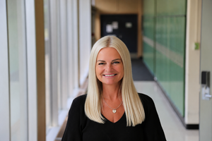 A white woman with blond hair smiling at the camera in a hallway