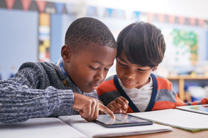 Two students look at a tablet together at a desk.