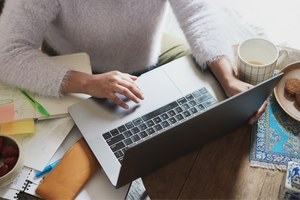 An aerial view of a laptop with coffee, food, and a notebook placed around.