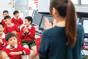 Students in red uniforms face a teacher in a classroom.