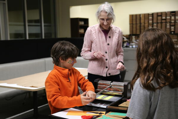A woman helping two students with a craft