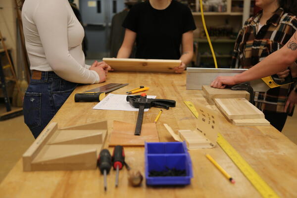 Students work around a workbench with hand saws and holding small cuts of wood.