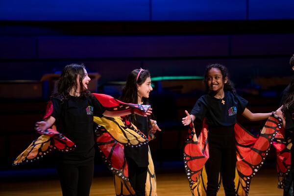 Three Sistema students wear butterfly wings and black shirts and pants.