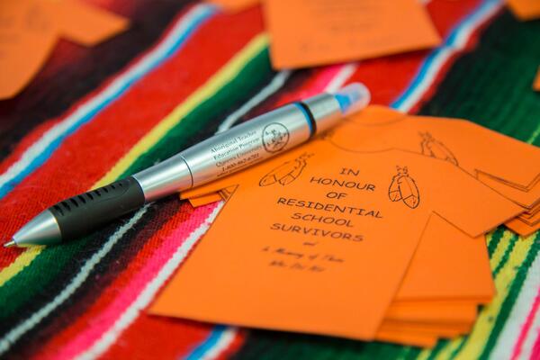 A small paper orange shirt with a pen on top of it