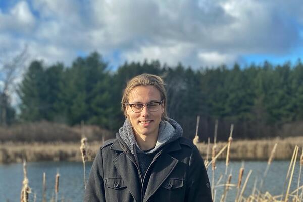 Jackson Pind smiles outside in front of a body of water.