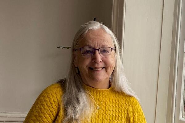 Jennifer Davis smiles inside against a white wall wearing a yellow sweater.