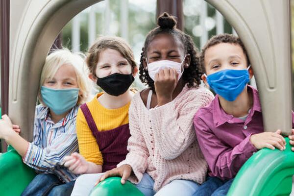 four young children smiling on a playground while wearing face masks