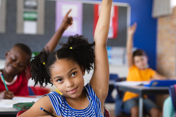 a group of kids raising their hands in a classroom
