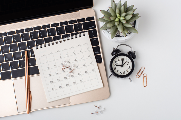 A laptop in a workstation with a calendar, clock, and plant