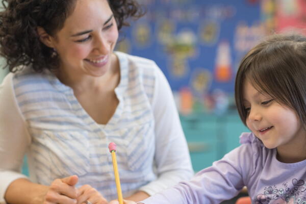 a teacher smiling at a child working in a classroom