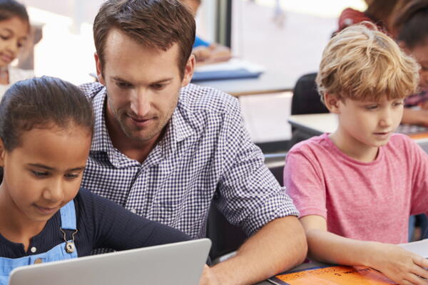 a teacher assisting students with a computer