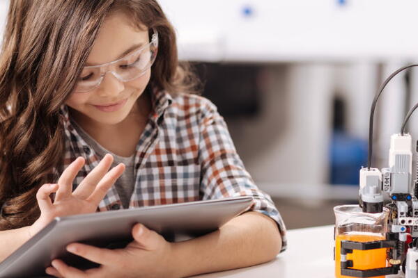a child working on their tablet next to a robot