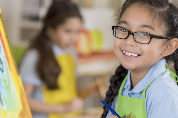 a child smiling at the camera standing in front of a canvas