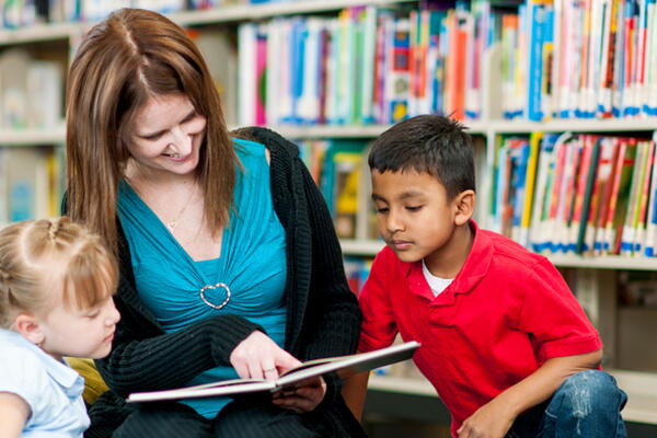 a teacher reading out a book to their students in a library