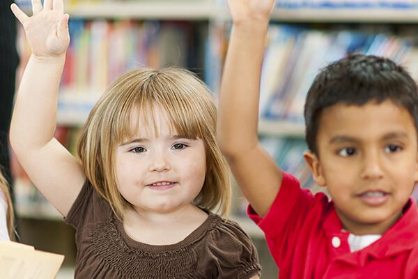 children raising their hands sitting in a library
