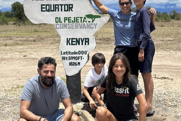 Jessica Hajee poses with her husband and children outside at an equator marker in Kenya.